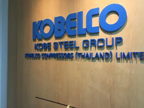 ตัวอักษรสีน้ำเงิน Kobelco บนผนังไม้