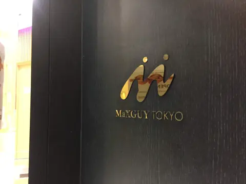 ป้ายโลโก้สีทอง Maxguy Tokyo บนผนังสีเข้ม