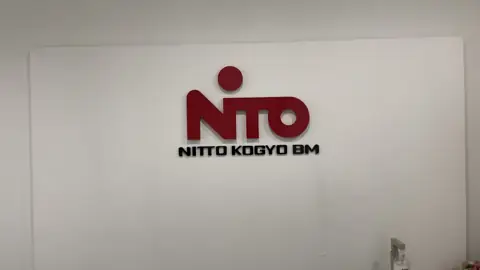 โลโก้ NITTO สีแดงบนผนังขาว